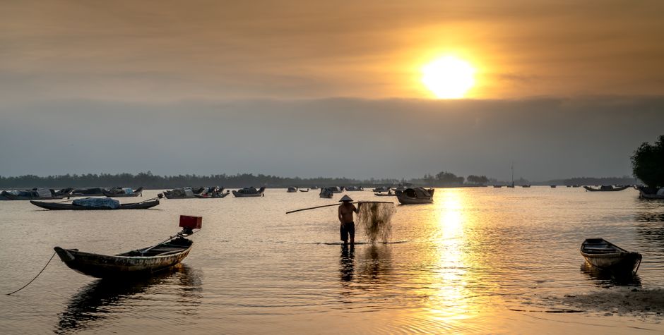A silhouette of a man fishing from a boat, casting his line into the water against a beautiful, golden sunrise over a calm sea.